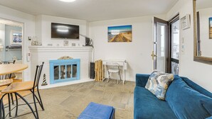 Ein Wohnzimmer mit blauem Sofa, Kamin, Esstisch mit Stühlen, Wand-Fernseher und einem Gemälde über dem Kamin.