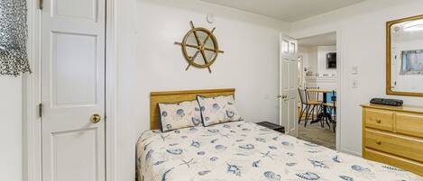 Un dormitorio con cama, cabecero de madera, una rueda de barco montada en la pared, cómoda y espejo.
