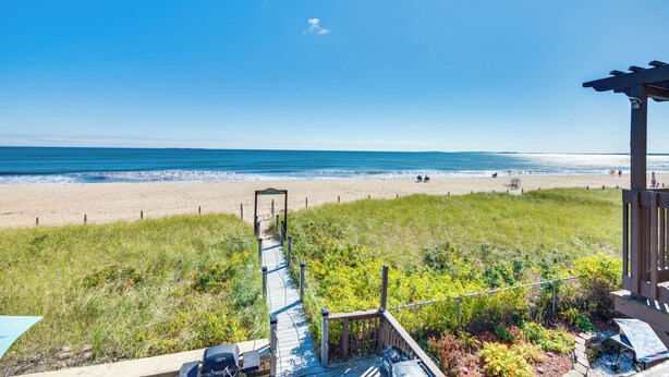 Blick auf einen Strand mit einer Holzterrasse, die zu einer Laube führt.