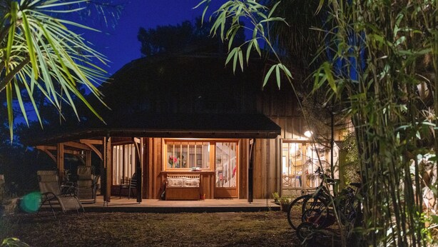 Een houten huis met een veranda, een eethoek en een keuken die door de ramen zichtbaar is.