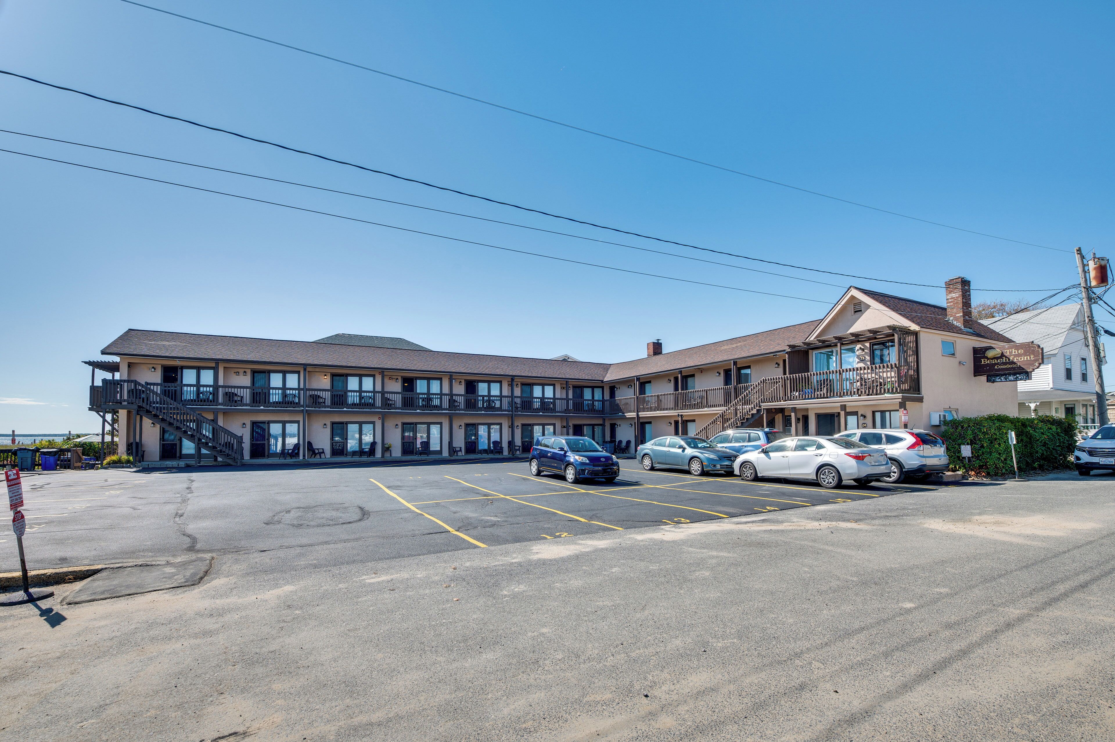 Un hotel a più piani con un parcheggio, diverse auto e un cielo azzurro intenso.