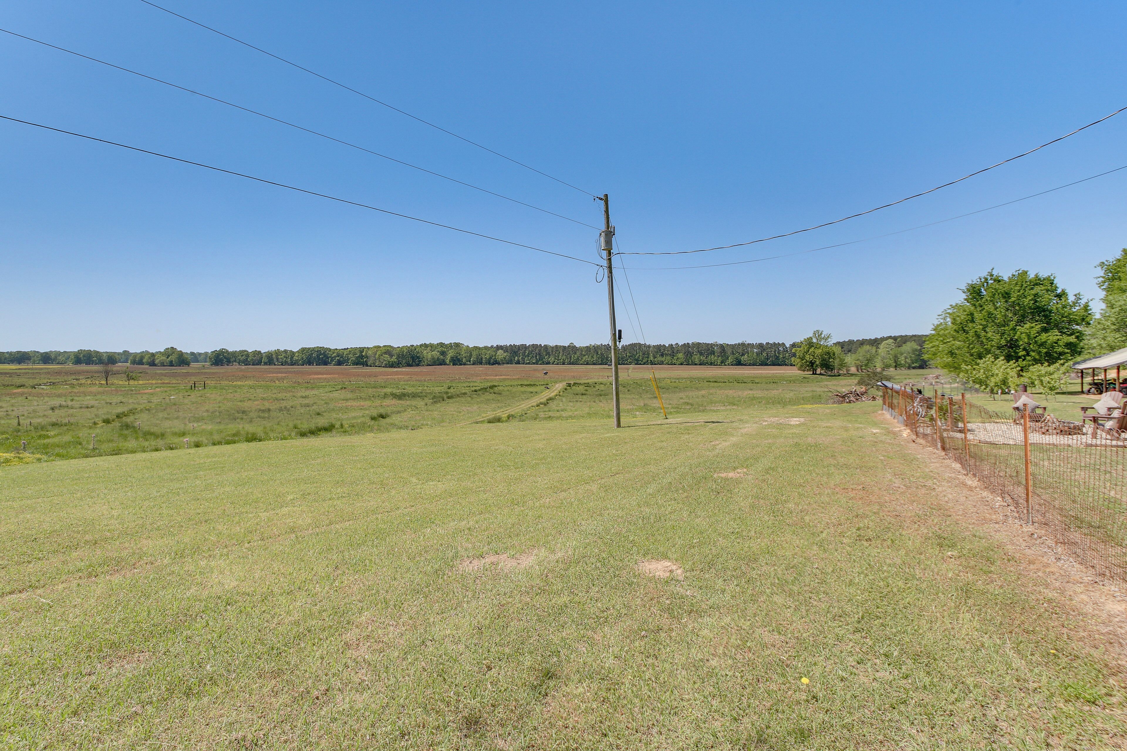 Un paysage rural avec un champ d’herbe, un poteau électrique et une zone délimitée par une clôture, à l’intérieur de laquelle se trouve un bâtiment.