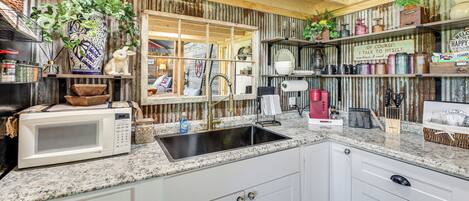 A kitchen with white cabinets, a granite countertop, a microwave, a sink, and various kitchen items.