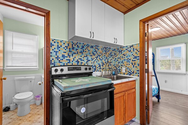 Une cuisine de taille réduite, avec un mur recouvert de carreaux, une cuisinière et des meubles de rangement en bois.