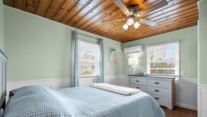 Un dormitorio con una cama, ventilador de techo, cómoda y dos ventanas con persianas.