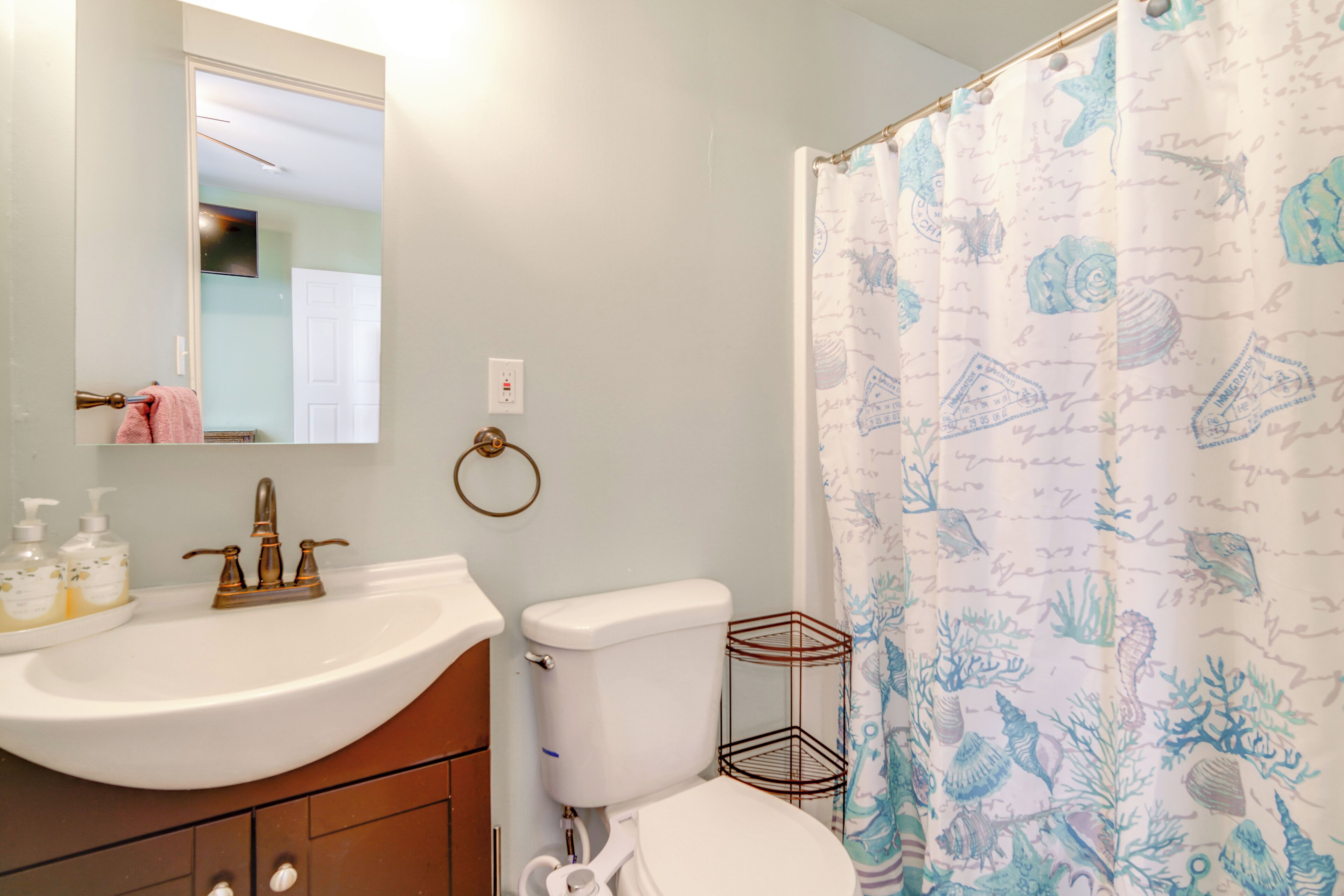 A bathroom with a white sink, a toilet, and a shower curtain with a sea-themed pattern.