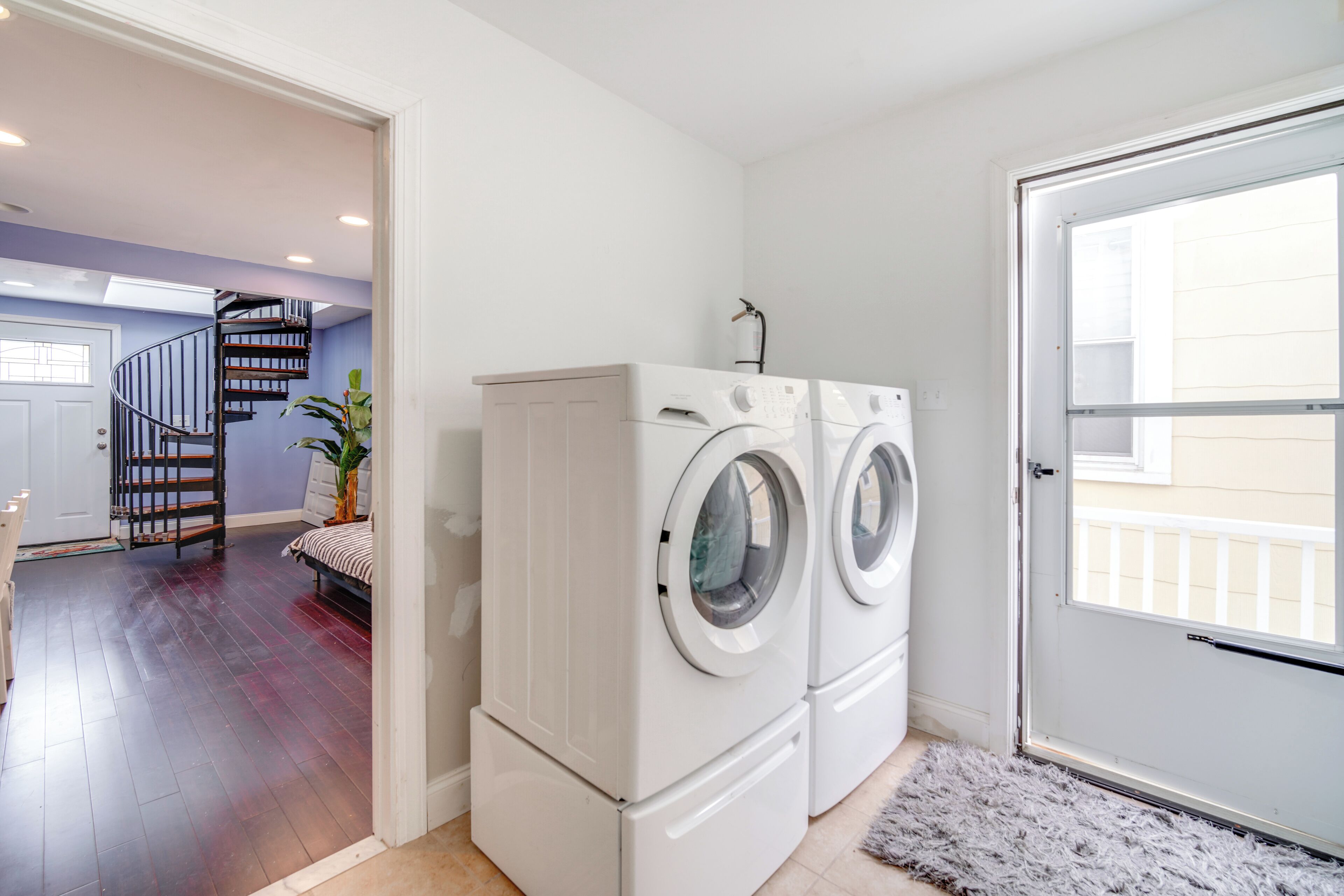 A laundry area with two stacked front-loading washers and dryers, a staircase leading to another room, and a door to the outside.
