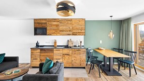 A modern kitchen with wooden cabinetry, a built-in microwave, and a dining area with a wooden table and chairs. - Deluxe Suite | Pool, sauna & mountain view (Reit im Winkl)