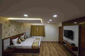 A hotel room with a large bed, a television, and a wooden floor. - White Stone Comfort (Bengaluru)