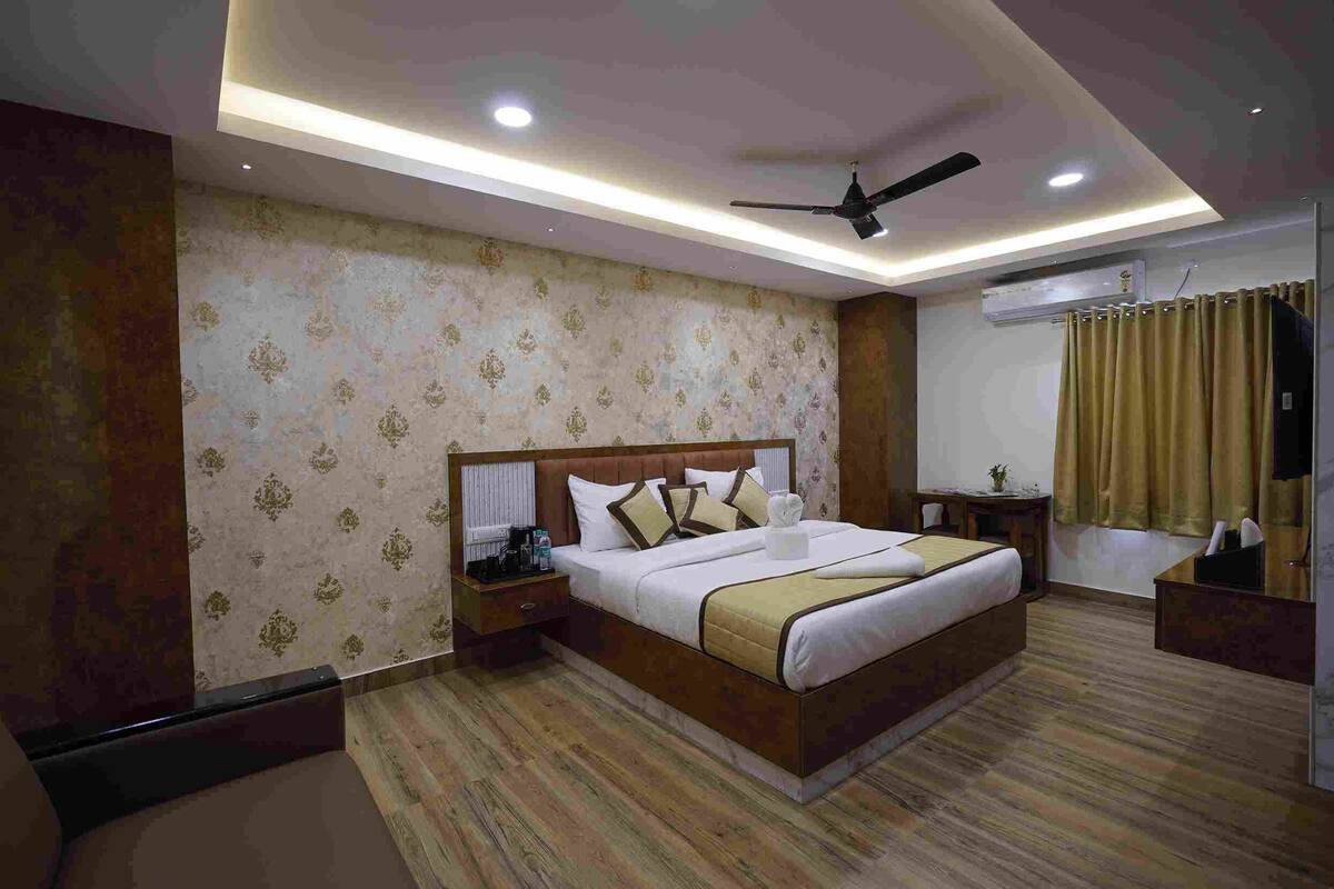 A hotel room with a large bed, a nightstand, a bedside table, a ceiling fan, and an air conditioning unit.
