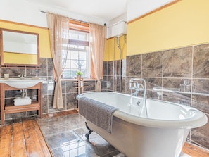 A modern bathroom with a freestanding bathtub, a vanity with a mirror, and a window with curtains. - 1 Cleator Gate (Cleator)