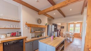 A kitchen with wooden beams, a dishwasher, a refrigerator, and a dining area with a table and chairs. - 1 Cleator Gate (Cleator)