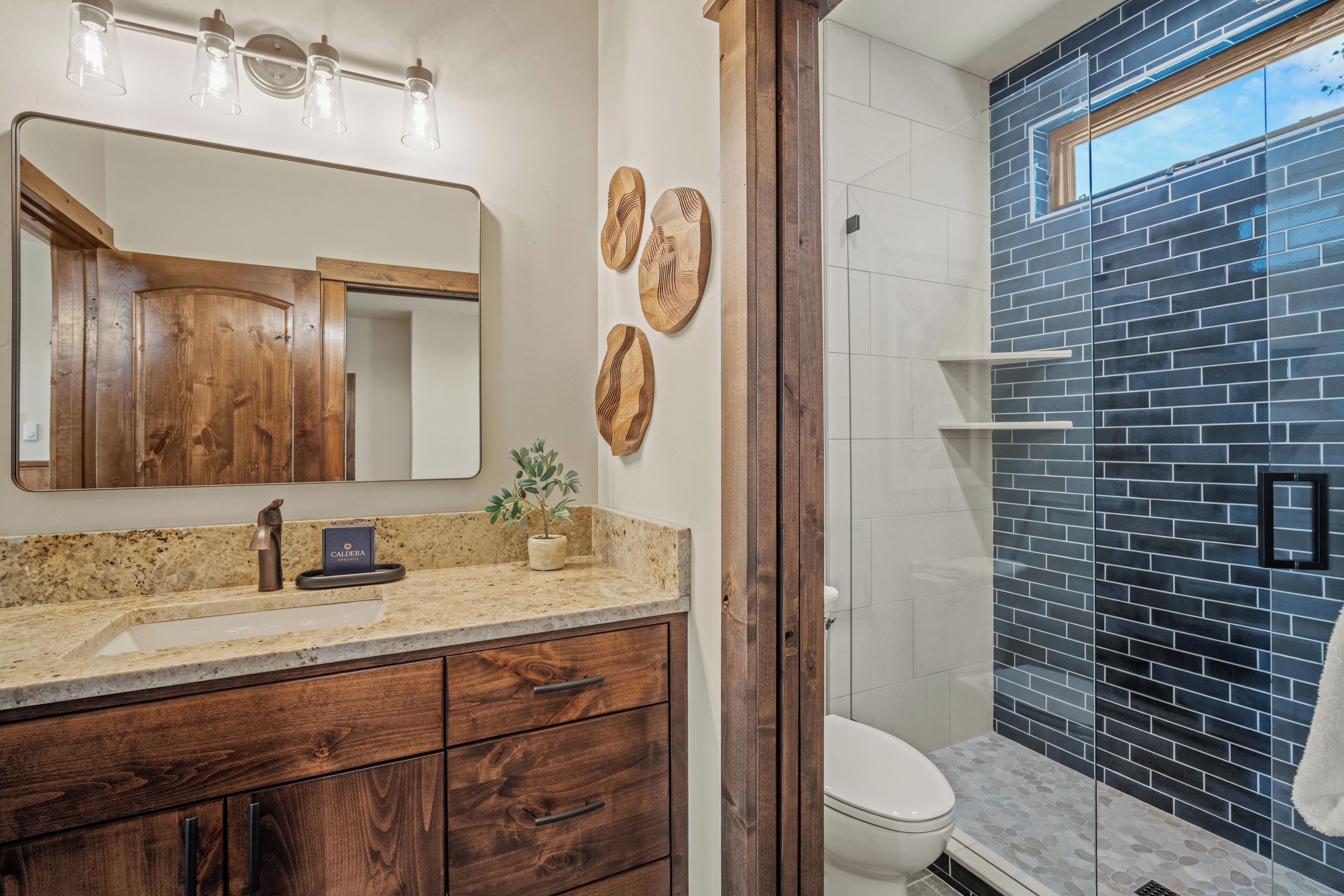 A bathroom with a wooden vanity, a large mirror, and a dark tiled shower area.