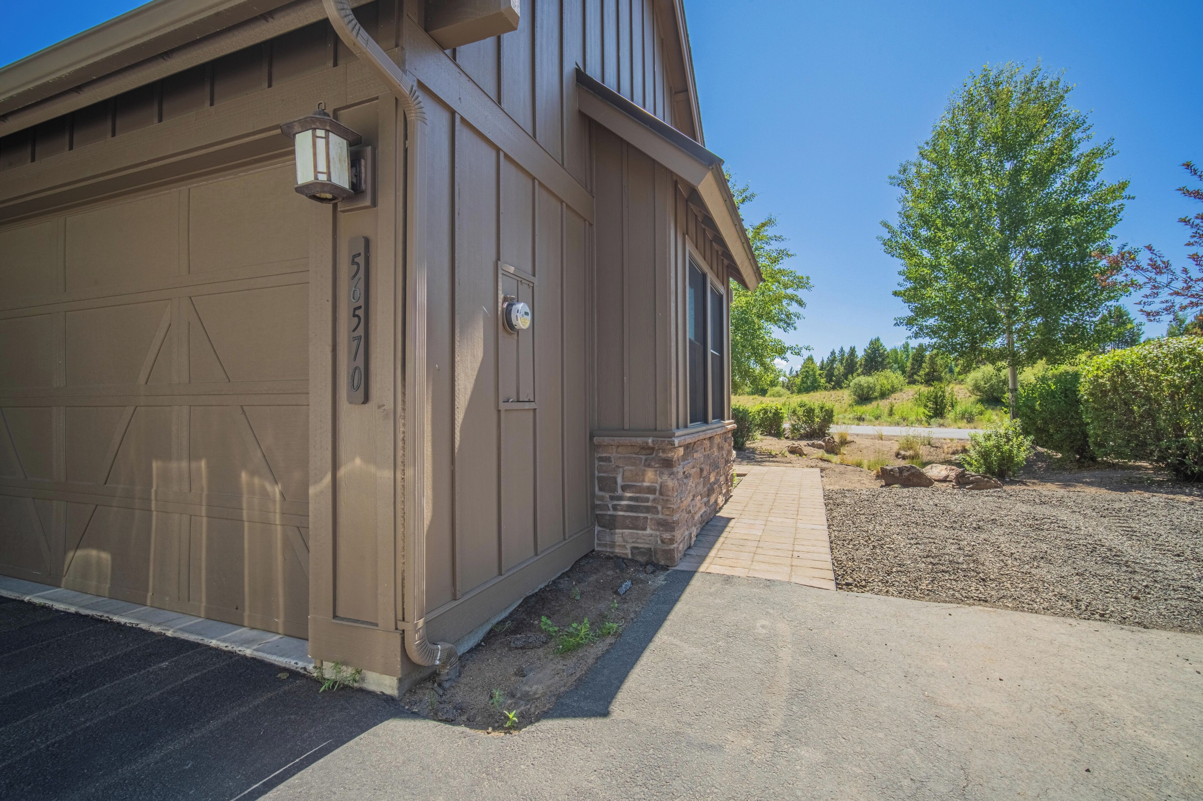 A residential building with a garage door, a stone foundation, and a landscaped driveway.