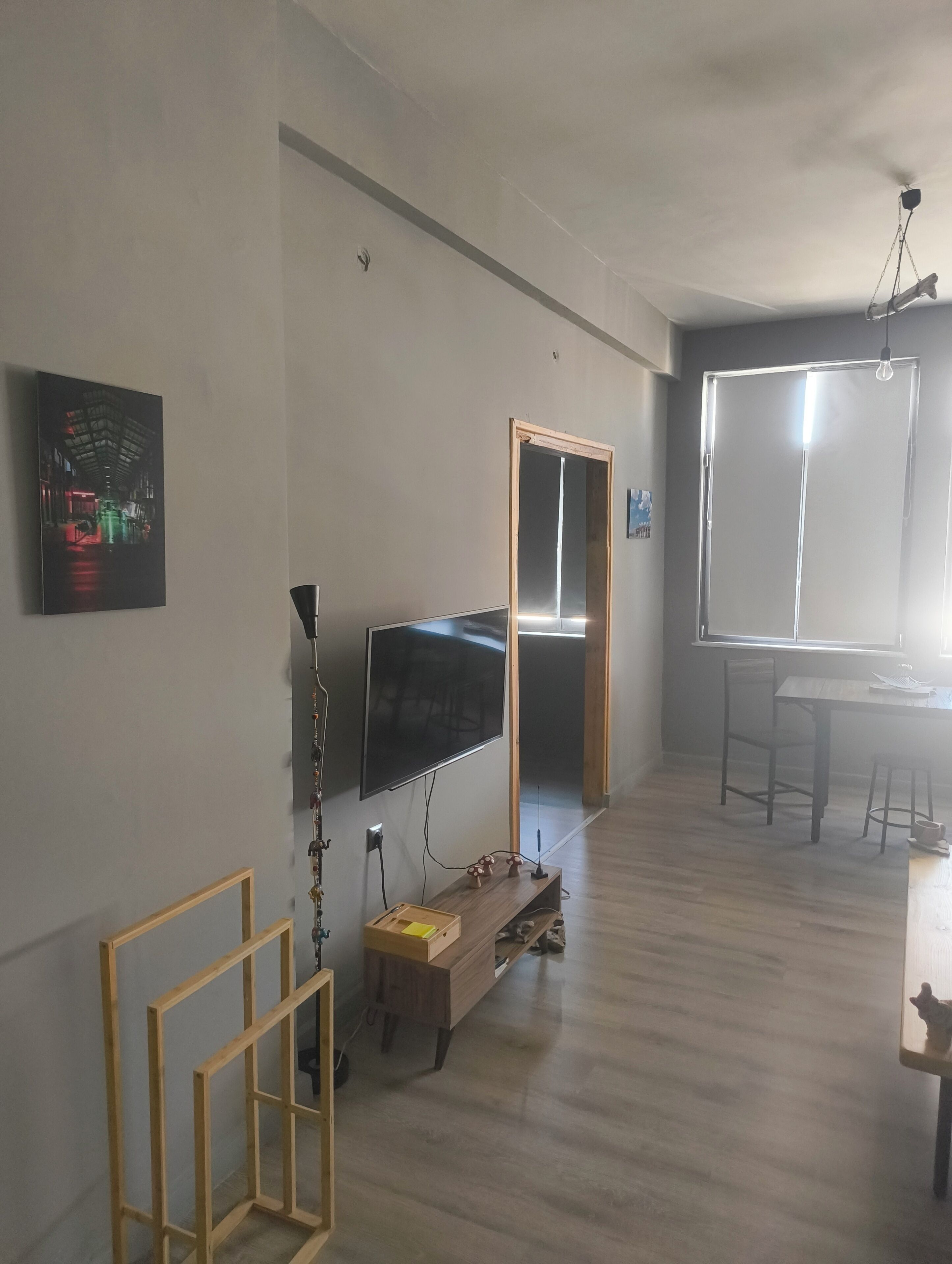 Ein Zimmer mit Flachbildfernseher an der Wand, einem Holzschrank, einem kleinen Hocker und einem Tisch mit Stühlen.