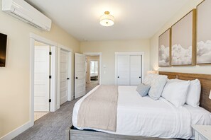 A bedroom with a large bed, a ceiling fan, and a wall-mounted air conditioner. - Seabrook King Tide | Oceanfront, Hot Tub, Pets 4BR | Sleeps 8, Pacific Landing (Pacific Beach)