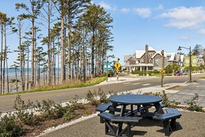 A picnic table by a road with a pedestrian crossing sign, a beach, and houses in the background. - Seabrook King Tide | Oceanfront, Hot Tub, Pets 4BR | Sleeps 8, Pacific Landing (Pacific Beach)