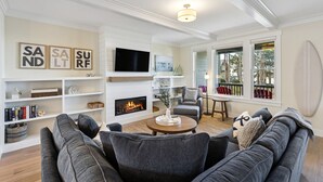 A modern living room with a fireplace, a television, and a balcony with red chairs. - Seabrook King Tide | Oceanfront, Hot Tub, Pets 4BR | Sleeps 8, Pacific Landing (Pacific Beach)