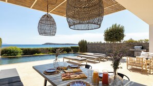 Een terras met buitenmeubilair en uitzicht op zee, een zwembad en een barbecue.