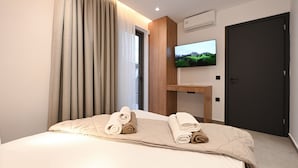 Une chambre d’hôtel avec un lit, un téléviseur à écran plat fixé au mur, une table de chevet en bois et une porte.