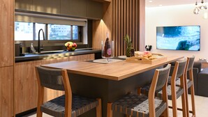 Une cuisine moderne avec des meubles en bois, un îlot central intégré et un grand téléviseur à écran plat fixé au mur.