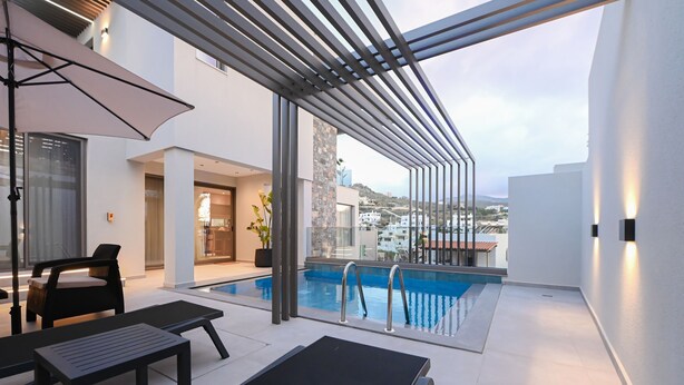 Un espace piscine extérieur moderne, doté d’une structure en verre, de chaises longues et offrant une vue sur les bâtiments environnants.