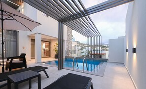 A modern outdoor pool area with a glass enclosure, lounge chairs, and a view of the surrounding buildings. - Luxury Suites With Private Swimming Pool 1st Floor (Malevizi)