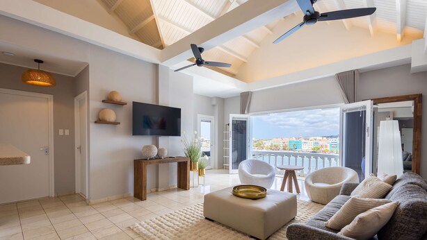 A modern living room with a large sofa, a TV, and a balcony with a view. - Chic City View Residence by the Bay (Willemstad)