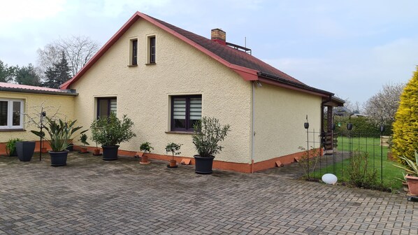 A single-story house with a red roof, beige walls, and a brick chimney. There are potted plants in front of the house and a paved driveway. - Private vacation apartment in Schulzendorf for 2-4 persons (Schulzendorf)