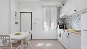 A compact kitchen with white cabinets, a microwave, and a window with curtains. - Lambrate Flat Milan (Milano)