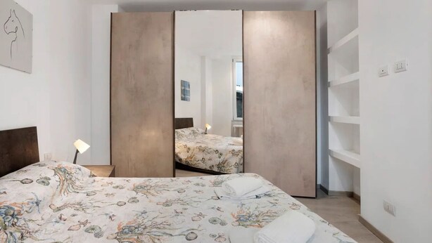 A bedroom with a bed, a nightstand, a lamp, a wardrobe, and a mirror. - Lambrate Flat Milan (Milano)