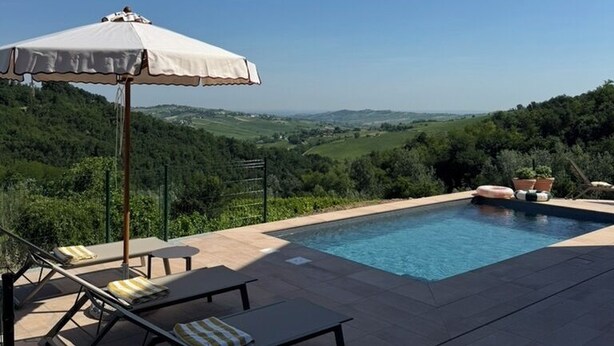 Une piscine dotée de chaises longues et d’un parasol, le tout situé dans un cadre paysager magnifique.