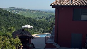 Un bâtiment rouge avec un toit en tuiles, une piscine et une vue sur un paysage verdoyant.
