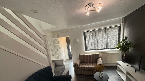 A modern living room with a staircase, a striped sofa, a black armchair, a small table, and a potted plant. - Close London City Airport- Petok - Free Parking (London)
