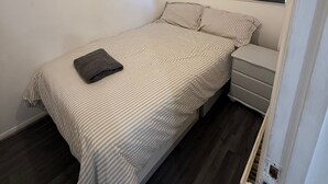 A small, neatly arranged bedroom with a bed, a nightstand, and a window with a blind. - Close London City Airport- Petok - Free Parking (London)