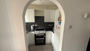 A compact kitchen with white cabinets, a black countertop, a stove, and a refrigerator. - Close London City Airport- Petok - Free Parking (London)