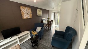 A modern living room with a flat-screen TV, two blue armchairs, a striped sofa, and a dining area with a table and chairs. - Close London City Airport- Petok - Free Parking (London)