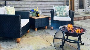 Une terrasse dotée de meubles en osier, d’un foyer extérieur et d’un pot à fleurs suspendu.