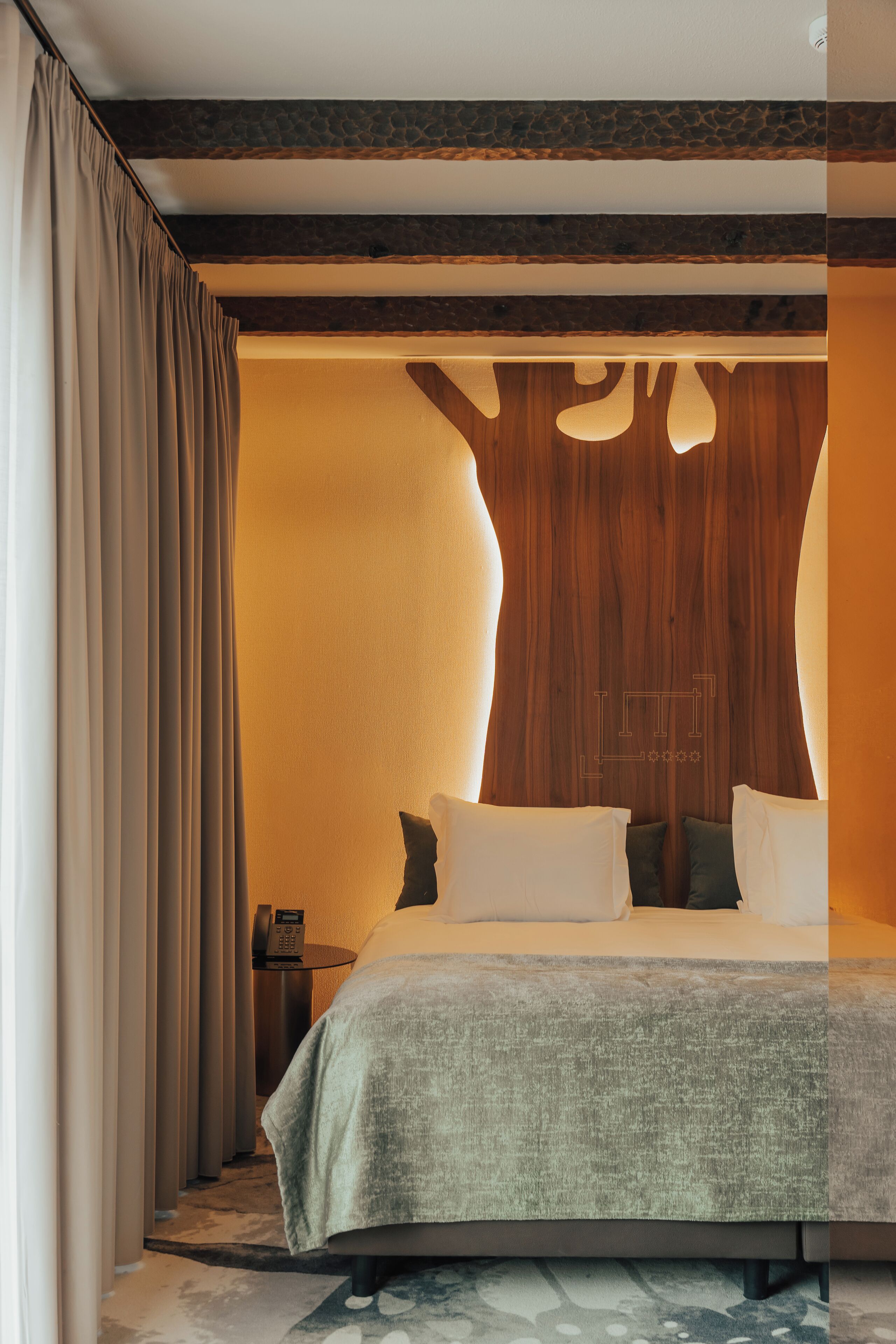 Una habitación de hotel moderna con una cama grande, un panel decorativo de madera y un teléfono sobre una mesita de noche.
