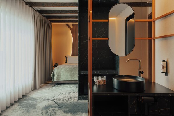 Habitación de hotel moderna con una cama grande, un espejo redondo, un lavamanos negro y un estante de madera.