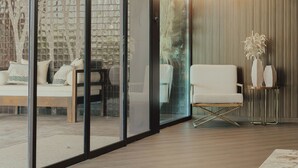 A modern hotel room with a glass partition, a sofa, a chair, and a decorative wall with a 'HOTEL' sign.