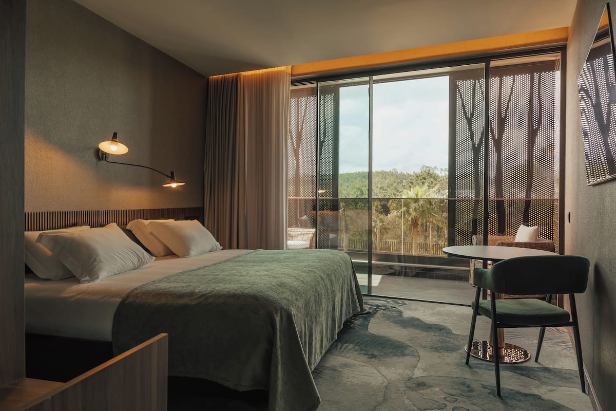 Une chambre d’hôtel comprenant un lit, une chaise, une table, un balcon avec vue et un luminaire fixé au mur.