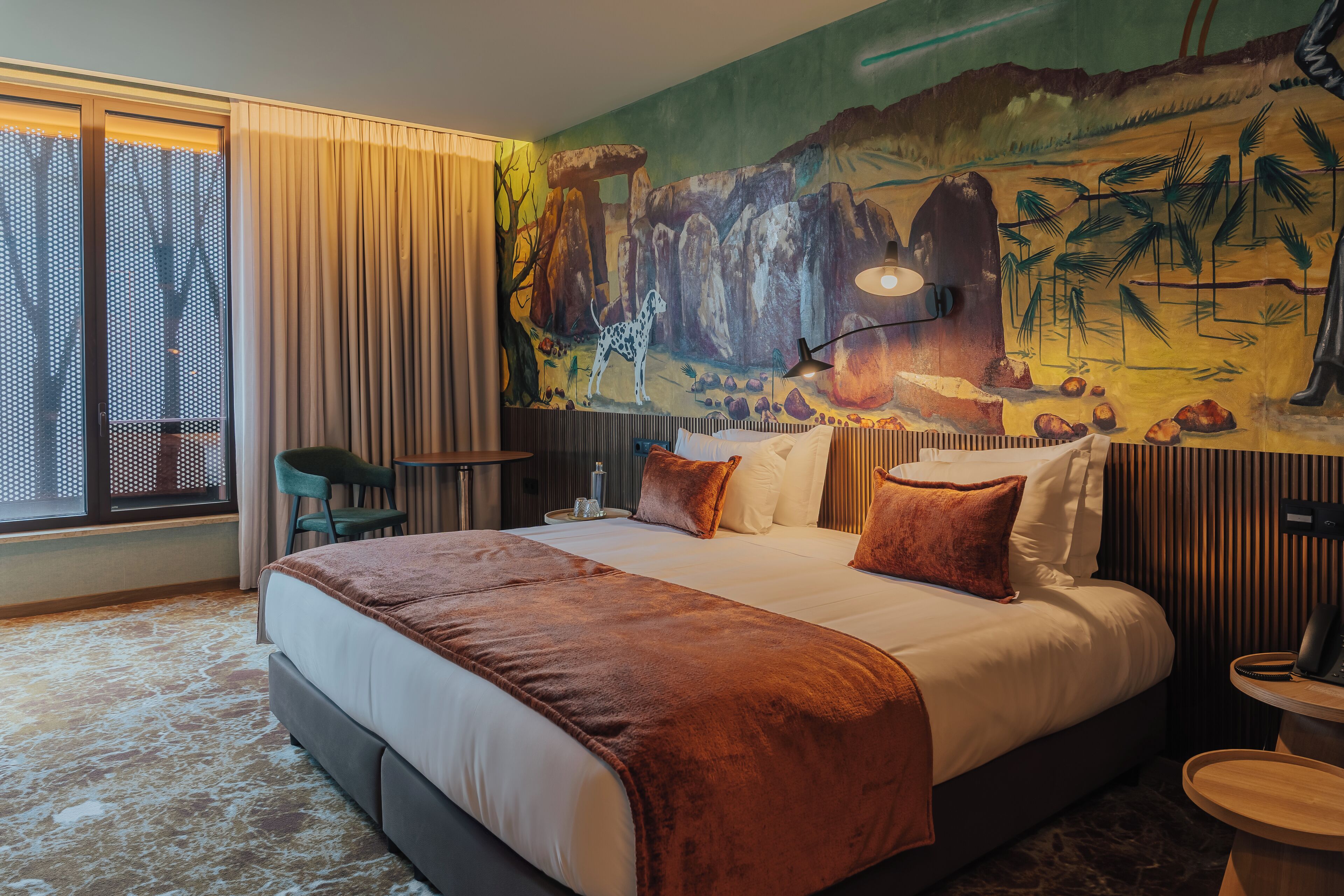 Een hotelkamer met een groot bed, een bureau, een stoel en een muurschildering.