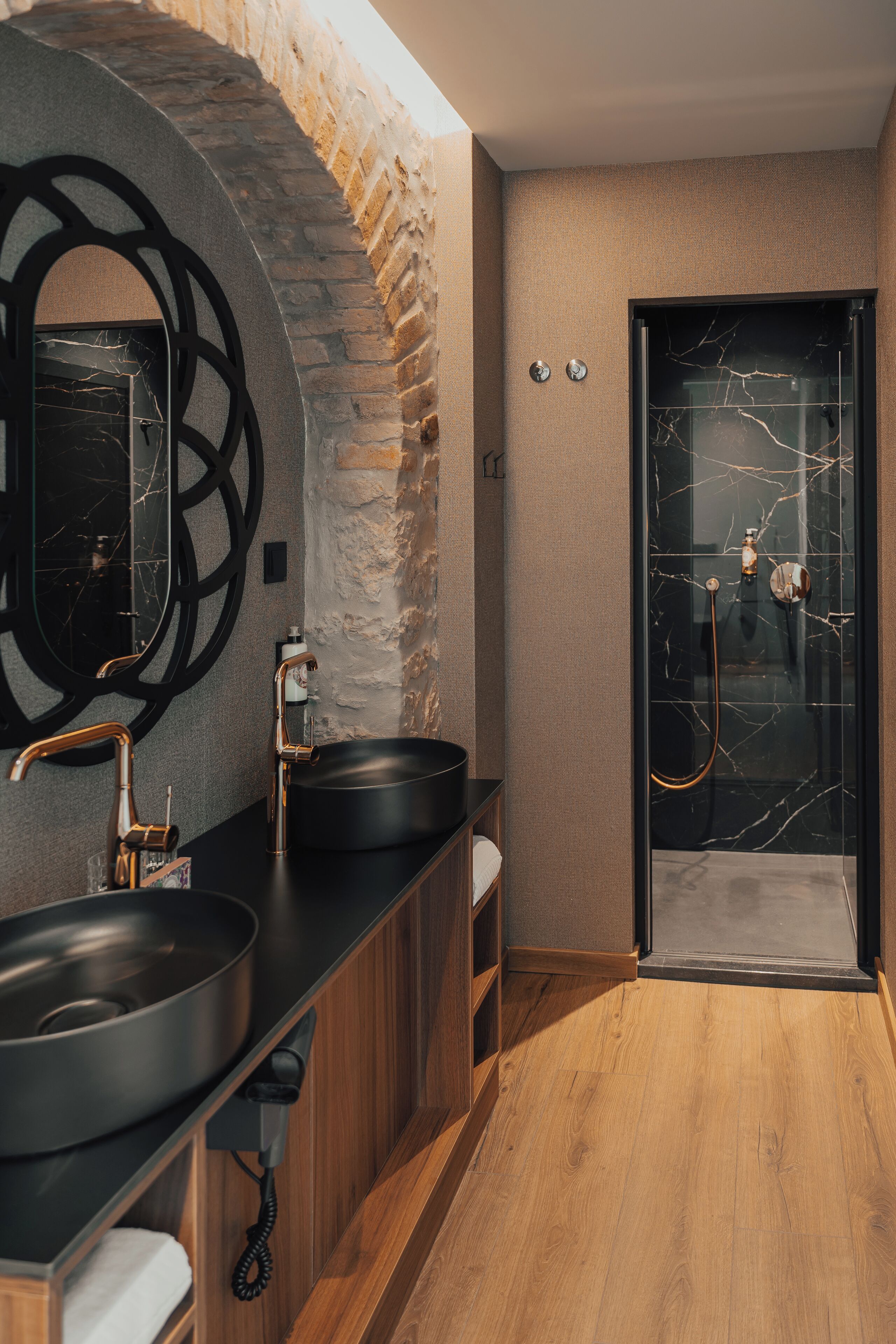 A modern bathroom with a large mirror, two sinks, a shower, and a wooden floor.