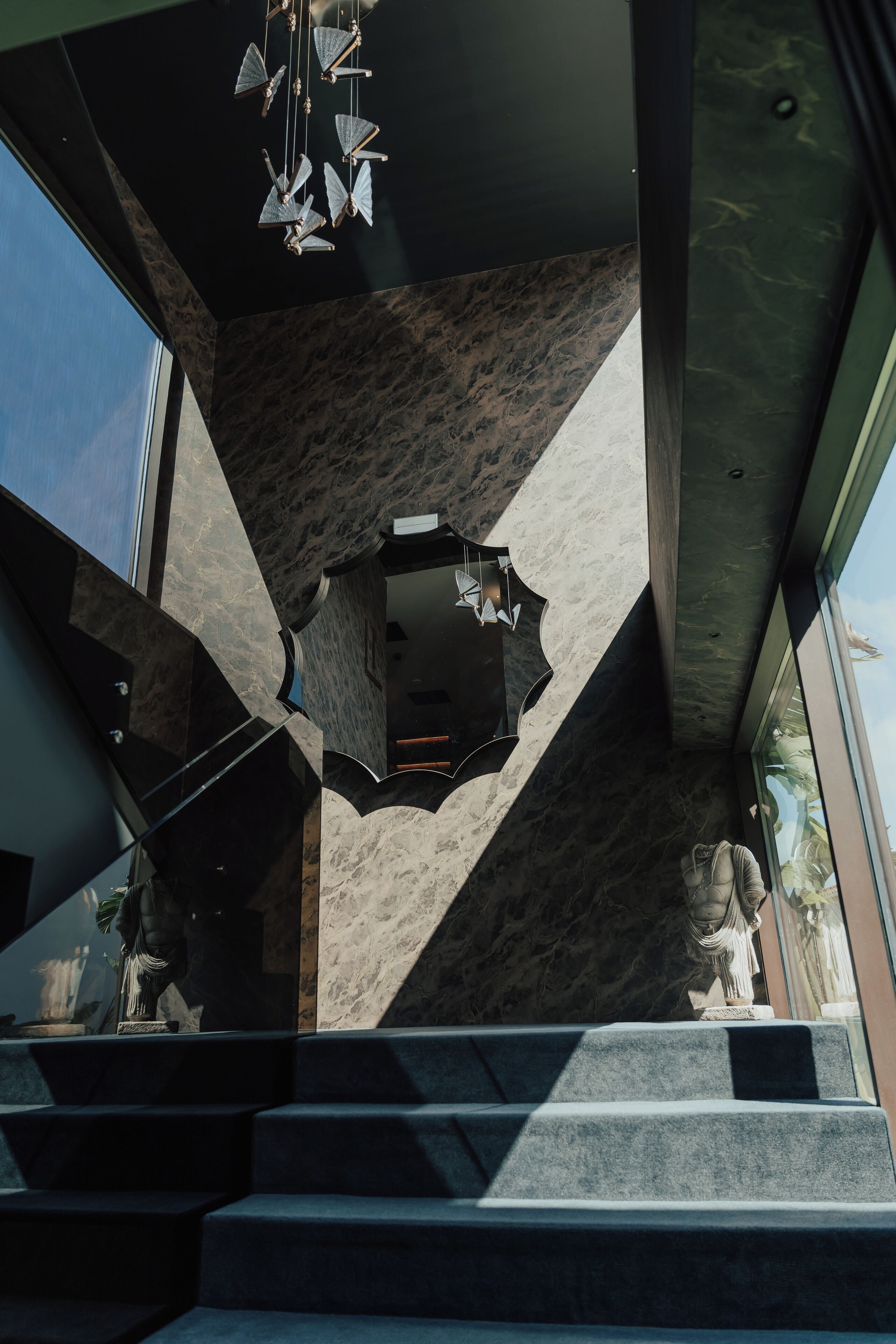 Un interior moderno con una pared de mármol geométrico, una escalera y una lámpara colgante.