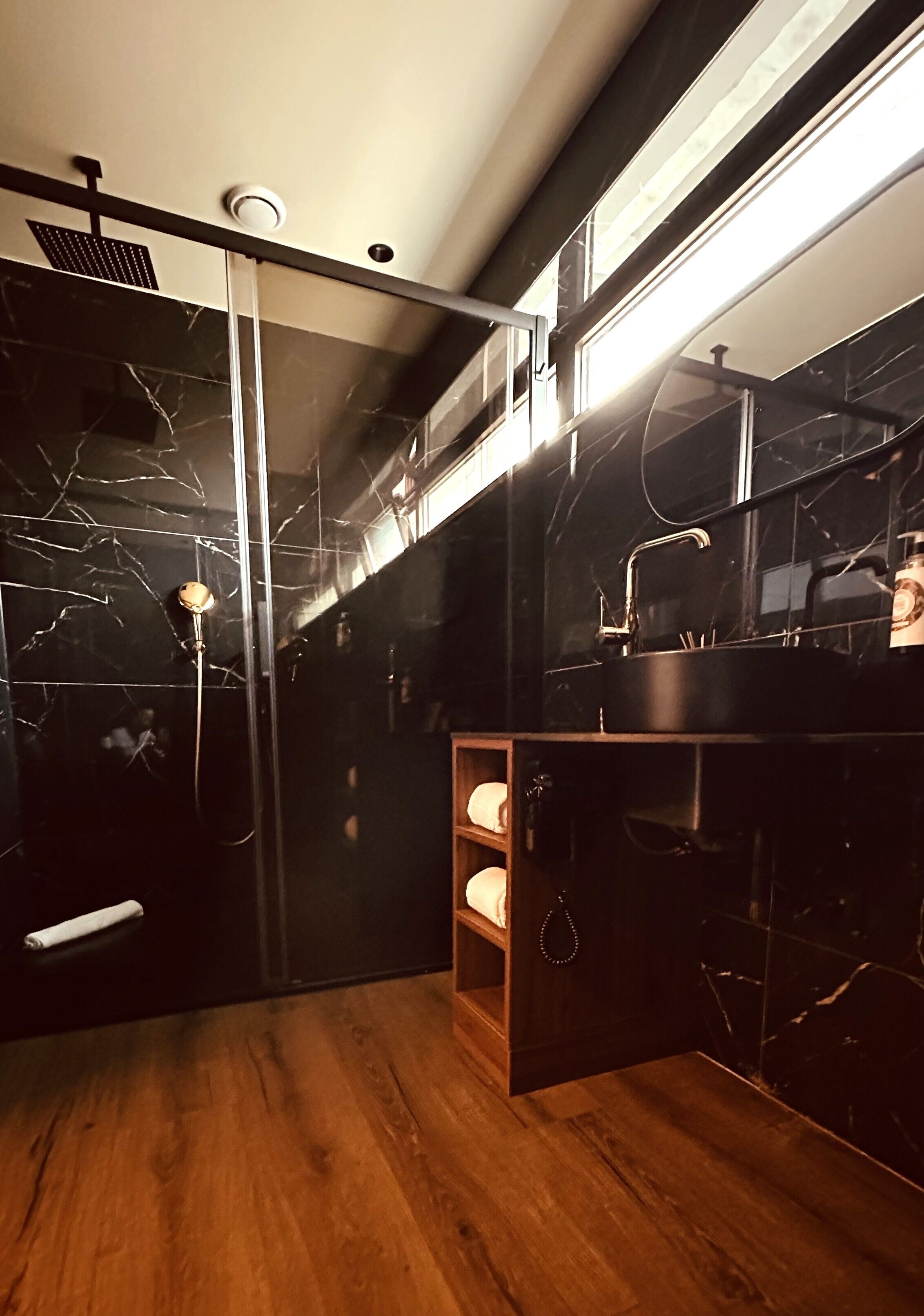 A modern bathroom with a glass shower enclosure, a wooden vanity with a sink, and a marble-tiled wall.
