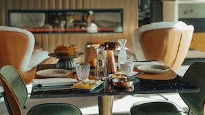 A dining table set with plates, glasses, and a coffee pot, surrounded by upholstered chairs.
