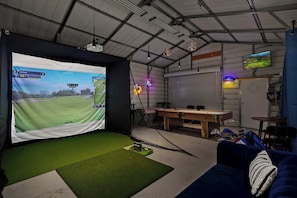 Una habitación con una pantalla grande mostrando un partido de golf, una mesa de billar y un sofá azul.