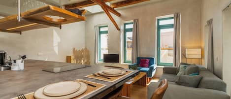 A modern kitchen with a wooden ceiling, a dining area with a table set for two, and a grey sofa in the living room.