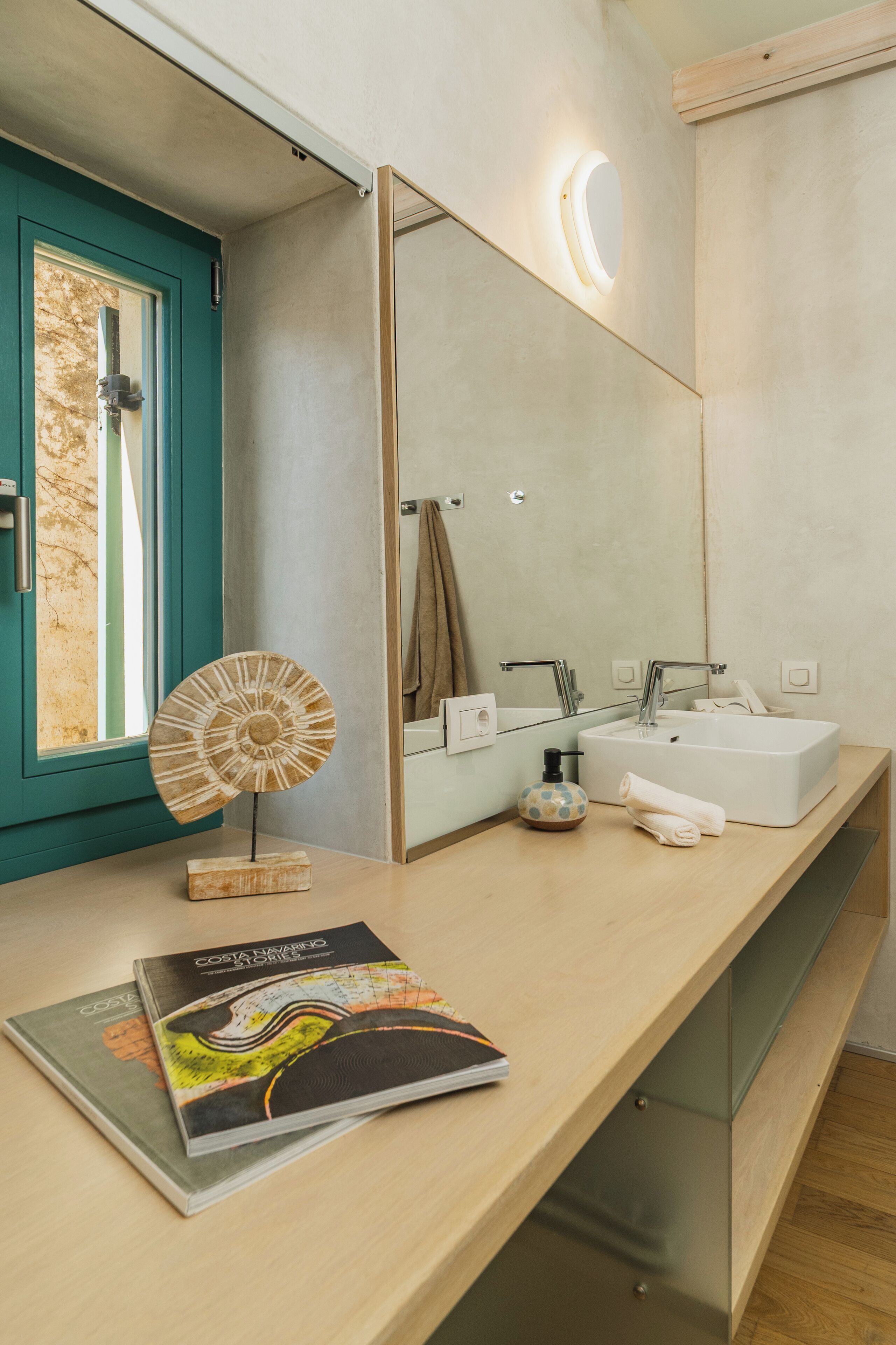 A modern bathroom with a large mirror, a sink, and a vanity. There is a decorative plate on the vanity and a magazine on the counter.